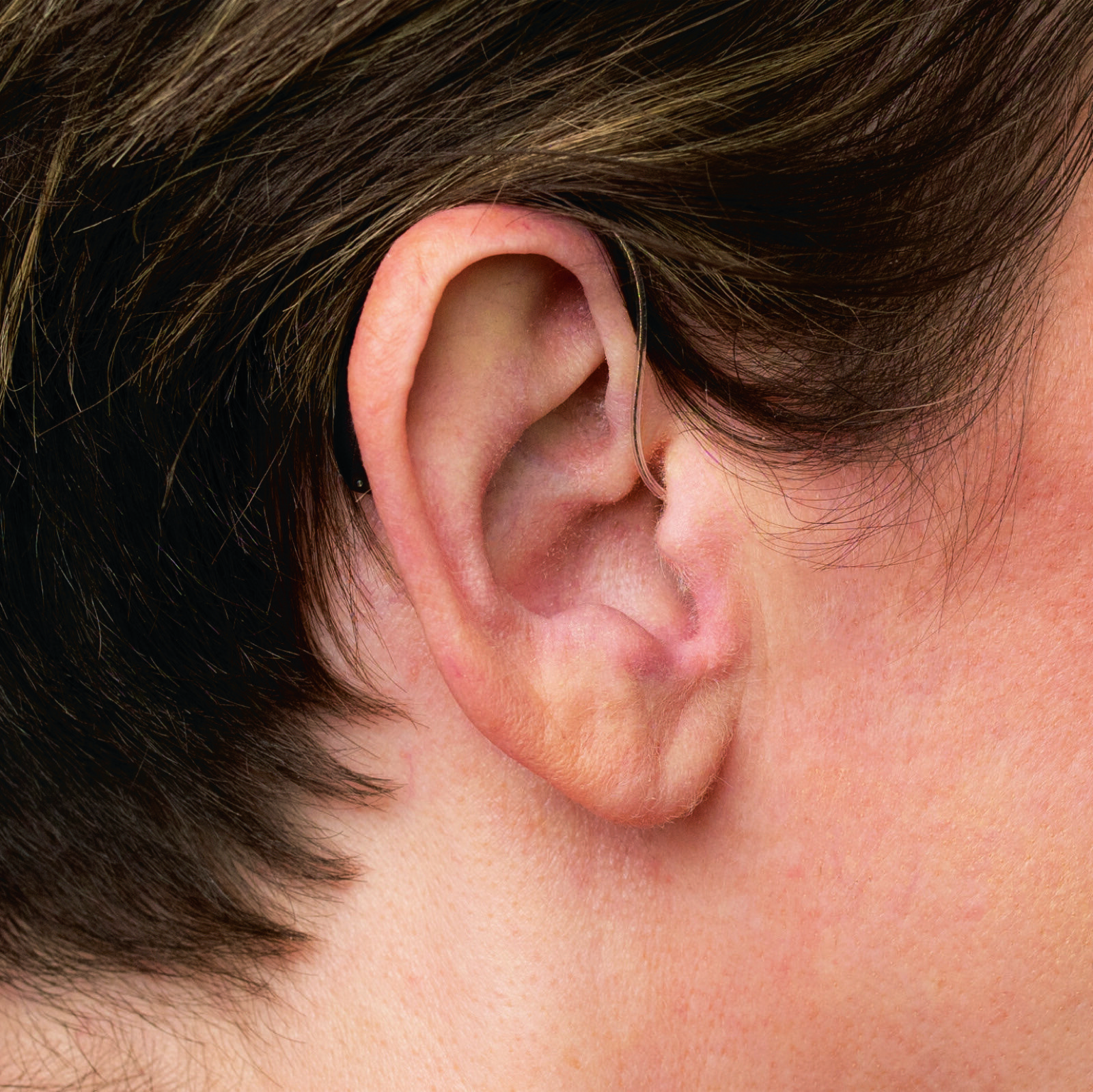 A Phonak Receiver-in-Canal hearing aid worn behind the ear, almost hidden by hair
